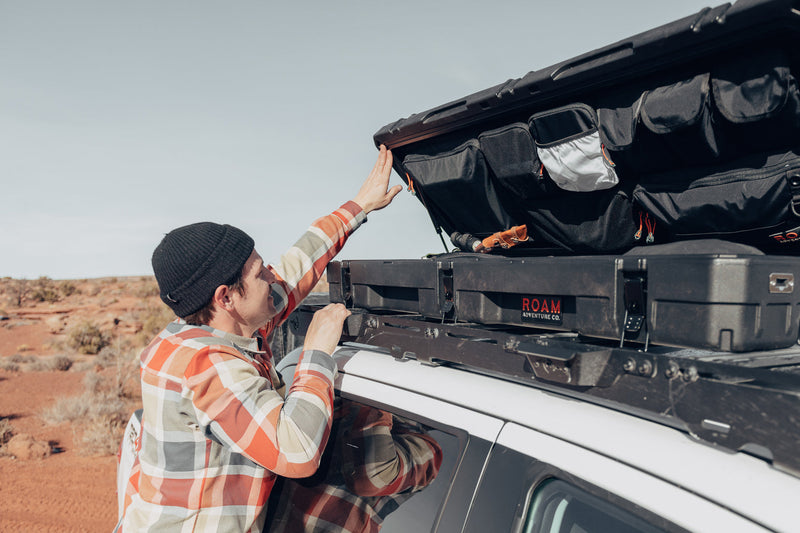 Load image into Gallery viewer, Man using the lid organizer of a low-profile 83L Rugged Case mounted on top of a vehicle
